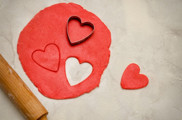 Pasta rossa con un mattarello e cuori tagliati su una tavola bianca, primo piano