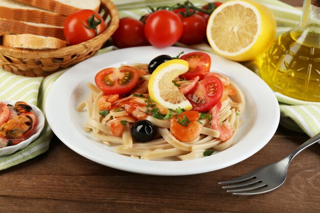 Pasta saporita con gamberetti cozze olive nere e salsa di pomodoro sul piatto su fondo di legno