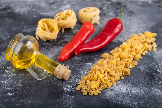 Pasta secca mista, peperoncino con bottiglia di olio d'oliva su marmo.