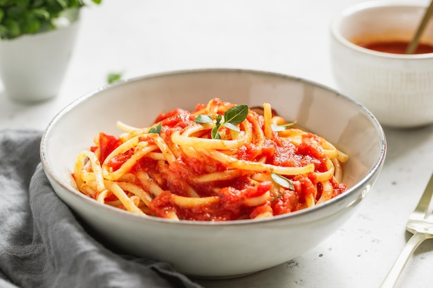 Pasta tradizionale con salsa di pomodoro e basilico greco in una ciotola di ceramica su un tavolo bianco