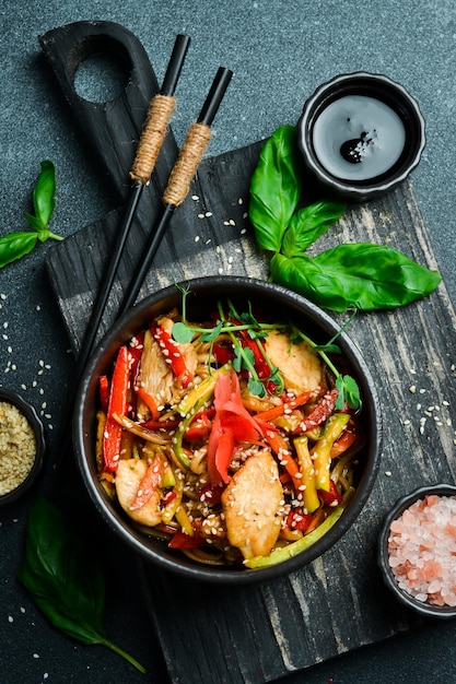Pasta Udon con pollo e zenzero in un piatto nero cucina giapponese su uno sfondo scuro da vicino