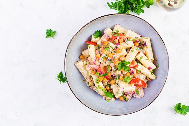 Pasta vegetariana alle verdure. Rigatoni di pasta con pomodoro, cipolla rossa, prezzemolo e ceci fritti con salsa di noci. Cibo vegano. Vista dall'alto, dall'alto