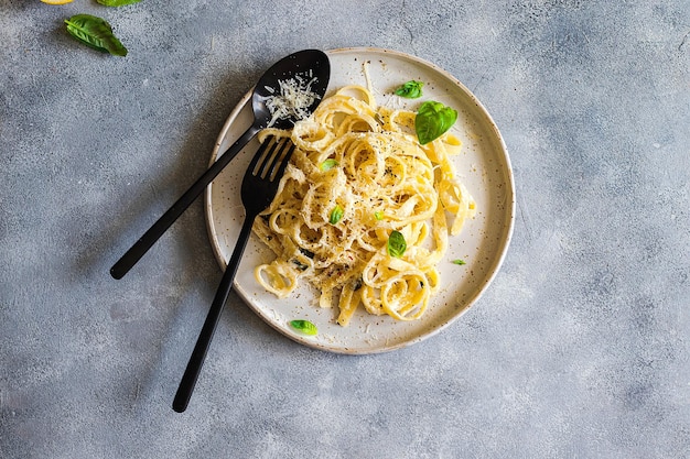 Pasta vegetariana con limone, basilico, parmigiano e pepe nero rosolata su fondo di pietra grigia. vista dall'alto con spazio di copia.