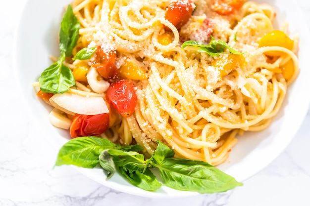 Pasta vegetariana con pomodorini e basilico fresco su un piatto bianco.