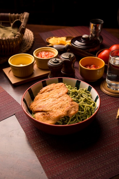 Pasta verde pesto di pollo filetto impanato cibo tradizionale peruviano mise en place tavola di legno