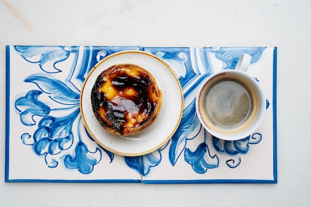 Pastel de nata. Dolce tradizionale portoghese, crostata di uova e tazza di caffè su piastrelle azulejo tradizionali su sfondo di marmo. Vista dall'alto