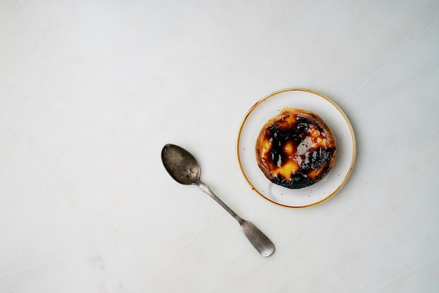 Pastel de nata. Dolce tradizionale portoghese, crostata di uova sul piatto in ceramica con cucchiaio su sfondo di marmo. Vista dall'alto