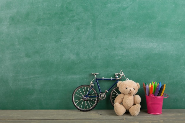 Pastelli colorati e orso giocattolo sul tavolo di legno concetto di educazione della scuola elementare lavagna sfondo