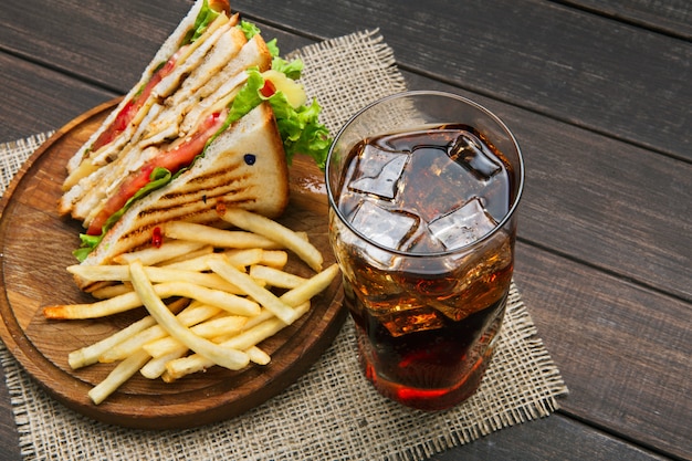 Pasti fast food al bar sandwich. Pollo e verdure sandwich, patatine e bicchiere di cola bere con ghiaccio su legno.