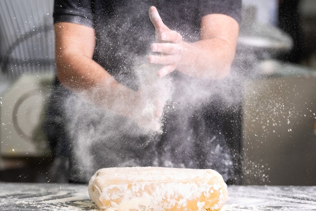 Pasticcere che applaude le sue mani con farina mentre produce la pasta