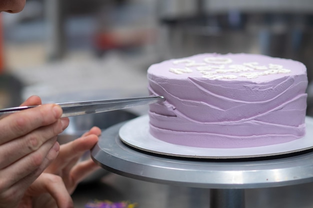 Pasticcere che decora una torta di compleanno glassata viola con granelli e perle di topping di testo