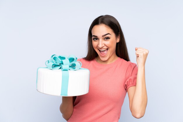 Pasticcere che tiene una grande torta isolata sulla parete blu che celebra una vittoria