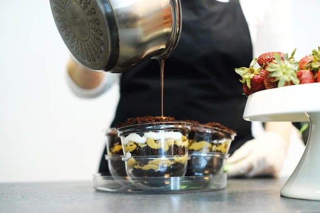 Pasticcere che versa cioccolata calda sopra il dessert a strati in forma trasparente