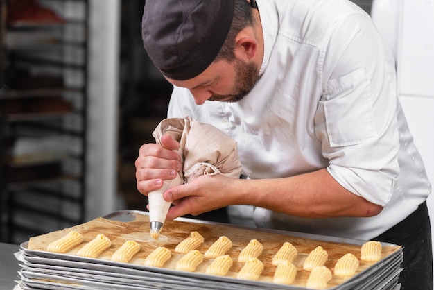 Pasticcere con il sacchetto della pasticceria che schiaccia crema alla pasticceria.