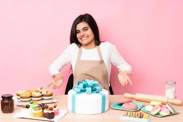 Pasticcere con una grande torta in una tabella sopra sorridente rosa isolato