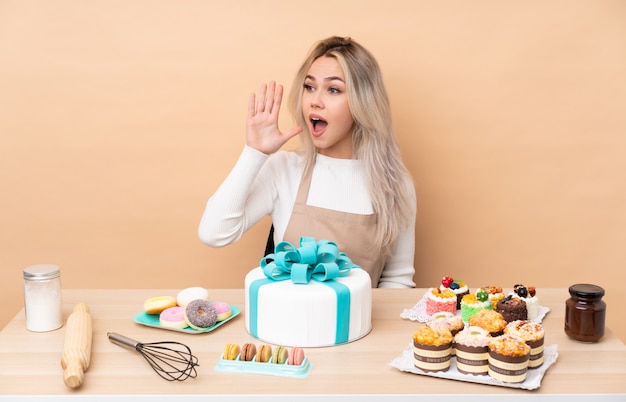 Pasticcere dell'adolescente con una grande torta in una tabella che grida con la bocca spalancata