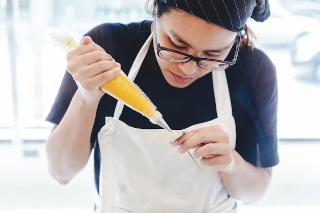 Pasticcere della donna che fa un fiore giallo del burro per la decorazione della torta.