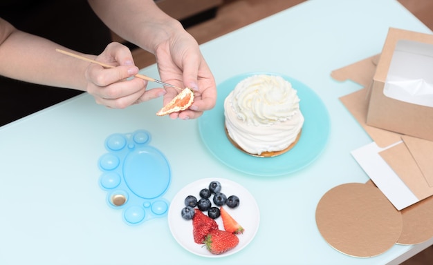 Pasticcere donna a casa che decora la torta di meringa fatta in casa Pavlova con frutti di bosco freschi estivi con fuoco selettivo Pasticceria fatta in casa deliziosi dolci concetto