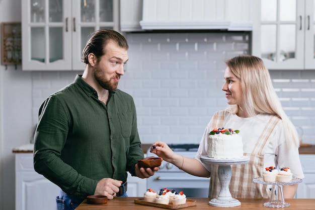 Pasticcere giovane donna caucasica con marito fidanzato uomo provare il gusto della torta sul tavolo da cucina Torte cupcakes e dessert dolce