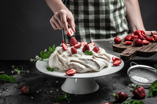 Pasticcere in cucina che decora la torta Torta Pavlova con fragole fresche e panna montata, concetto culinario, da forno, cibo e persone