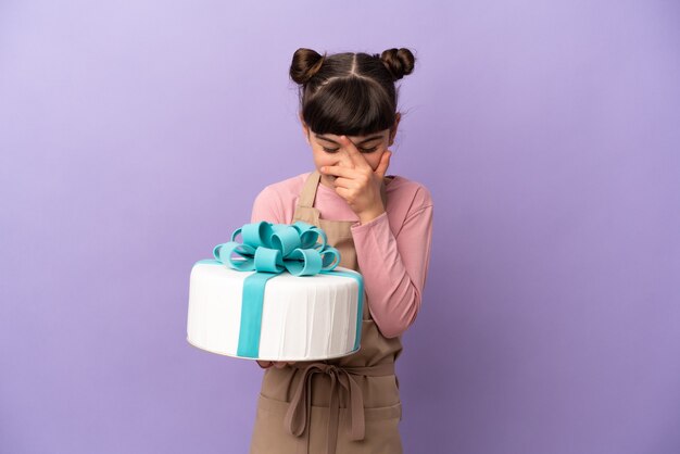 Pasticceria bambina tenendo una grande torta isolata su sfondo viola ridendo