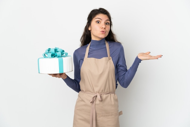 Pasticceria chef russo che tiene una grande torta isolata su priorità bassa bianca che ha dubbi mentre solleva le mani