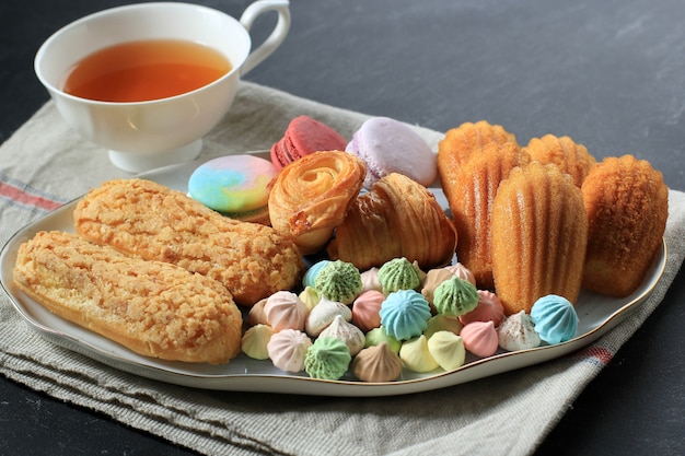 Pasticceria francese assortita con spazio copia su tavolo in marmo bianco per testo o ricetta. Amaretti, Meringa, Madeleine, Craquelin Eclair, Mini Croissant, Biscotti Grandi Al Cioccolato E Una Tazza Di Tè