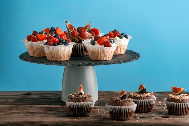 Pasticceria in stand. Muffin alla vaniglia e cioccolato con frutti di bosco freschi su sfondo blu. Vista laterale, copia spazio.