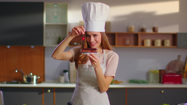 Pasticciere mettendo ciliegina sulla torta in cucina Donna sorridere alla telecamera