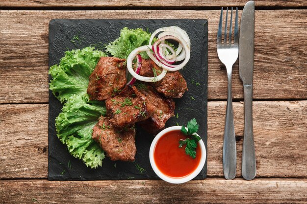 Pasto alla griglia appetitoso. Shashlik servito con insalata e anelli di cipolla su insalata nera con salsa di pomodoro, vista dall'alto.