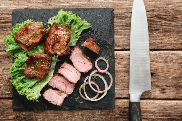 Pasto alla griglia appetitoso. Shashlik servito con insalata verde e anelli di cipolla su slade nera, su tavola in legno rustico.