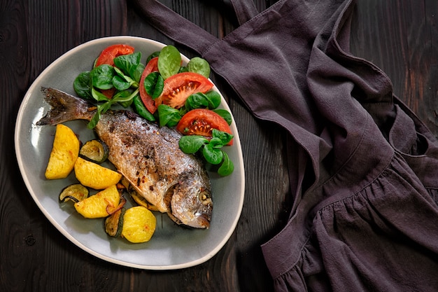 Pasto. Pesce Dorado al forno con verdure al forno su uno sfondo scuro.