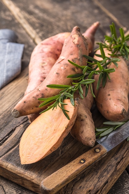 Patata dolce sul fondo del bordo di legno, fine su. Patate dolci crude o batatas alle erbe