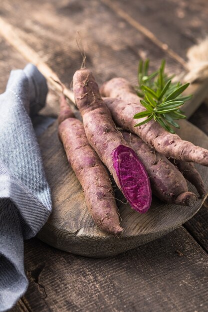 Patata dolce sul fondo del bordo di legno, fine su. Patate dolci crude o batatas alle erbe