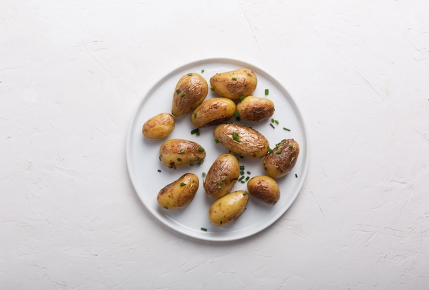 Patata novella al forno con la cipolla verde sul piatto bianco