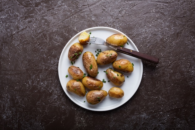 Patata novella al forno con la cipolla verde sul piatto bianco