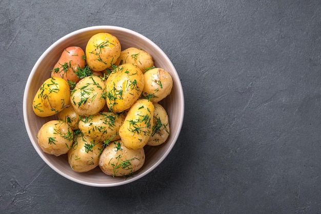 Patate bollite con la buccia con aneto fresco e olio su fondo di grafite