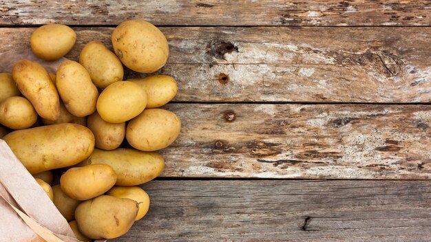 Patate crude che fuoriescono da un sacchetto di carta riciclato su assi di legno.