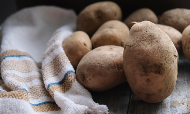 Patate crude fresche da terra nella cucina rustica con un canovaccio marrone e bianco