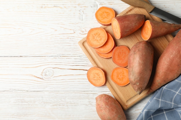 Patate dolci, coltello, tavola e asciugamano su superficie di legno