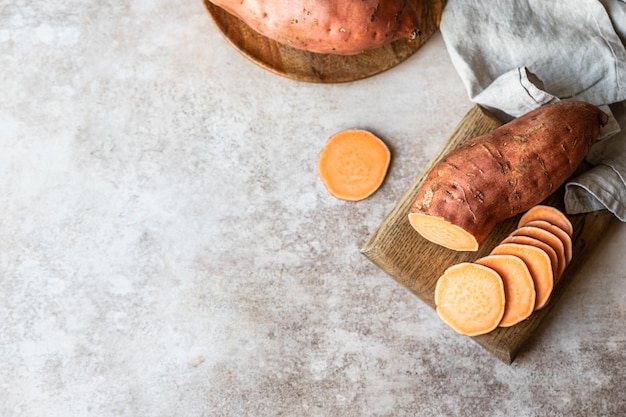 Patate dolci crude intere e affettate su tavola da cucina in legno igname biologico Il cibo della fattoria