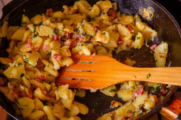 Patate domestiche arrostite in una padella con il primo piano della spatola di legno