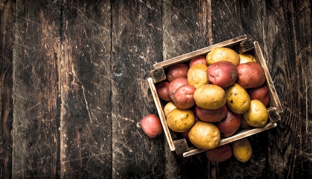 Patate fresche in una scatola di legno. Su uno sfondo di legno.