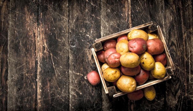 Patate fresche in una scatola di legno. Su uno sfondo di legno.