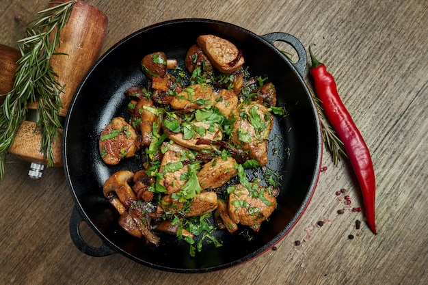 Patate fritte con carne di maiale, cipolle ed erbe in una padella decorativa su una superficie di legno. Vista dall'alto su cibo gustoso.