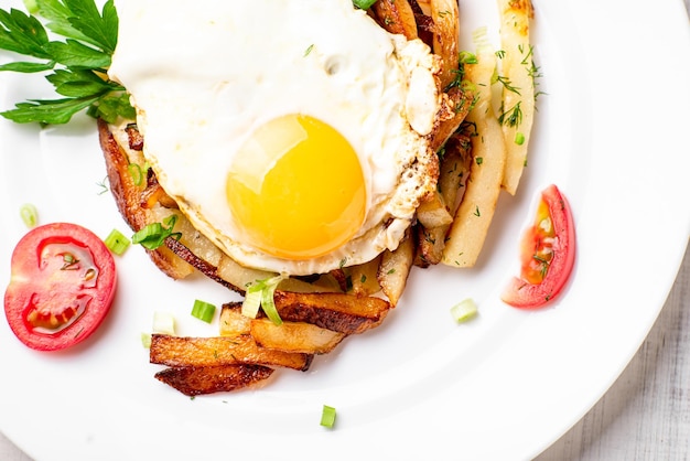 Patate fritte con erbe aromatiche e pomodori su un piatto bianco su fondo di legno bianco