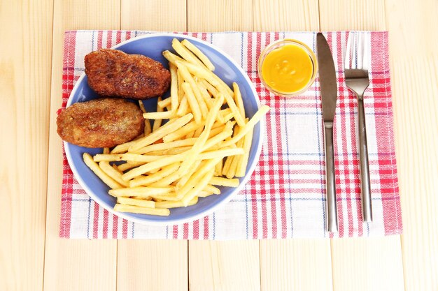 Patate fritte con hamburger sul piatto su sfondo in legno