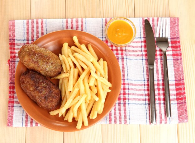 Patate fritte con hamburger sul piatto sul primo piano del tavolo di legno