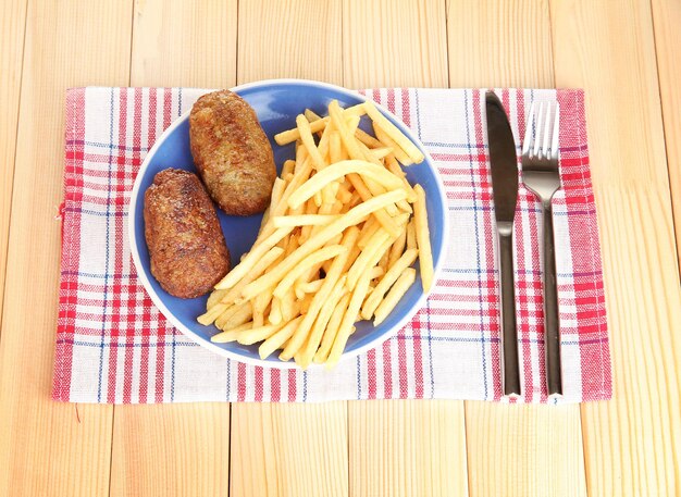 Patate fritte con hamburger sul piatto sullo sfondo in legno