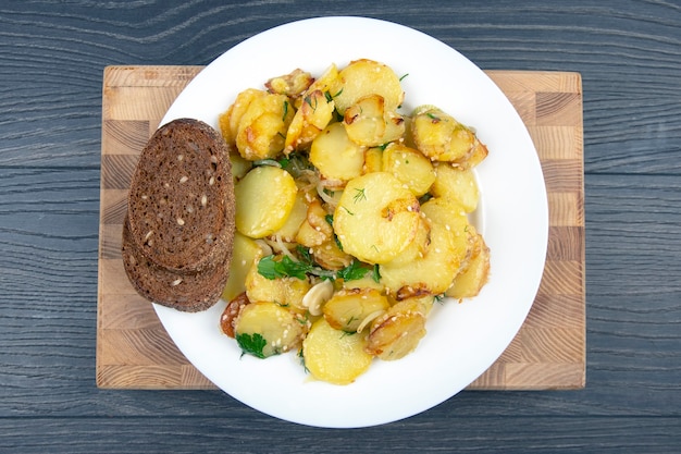 Patate fritte cotte con erbe e verdure in un piatto bianco su un tavolo di legno, vista dall'alto